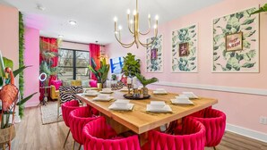 A dining area with a wooden table, red upholstered chairs, and tropical-themed wall art.