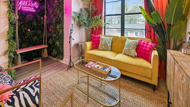 A modern living room with a yellow sofa, a glass coffee table, a neon sign, and a large window.