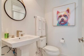 A bathroom with a white sink, toilet, and a framed painting of a dog. - Good Vibes Only - Walkable to breweries, cafes, restaurants & close to Broadway (Nashville)