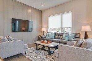 Un salon moderne avec un téléviseur à écran plat fixé au mur, un canapé gris avec des coussins bleus, une table basse avec un plateau et un tapis à motifs.