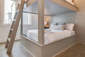 A bedroom with a built-in bed, a ladder, and a nightstand with a lamp.