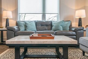 Ein Wohnzimmer mit einem grauen Ledersofa, einem Marmortisch und je einer Lampe auf beiden Seiten.