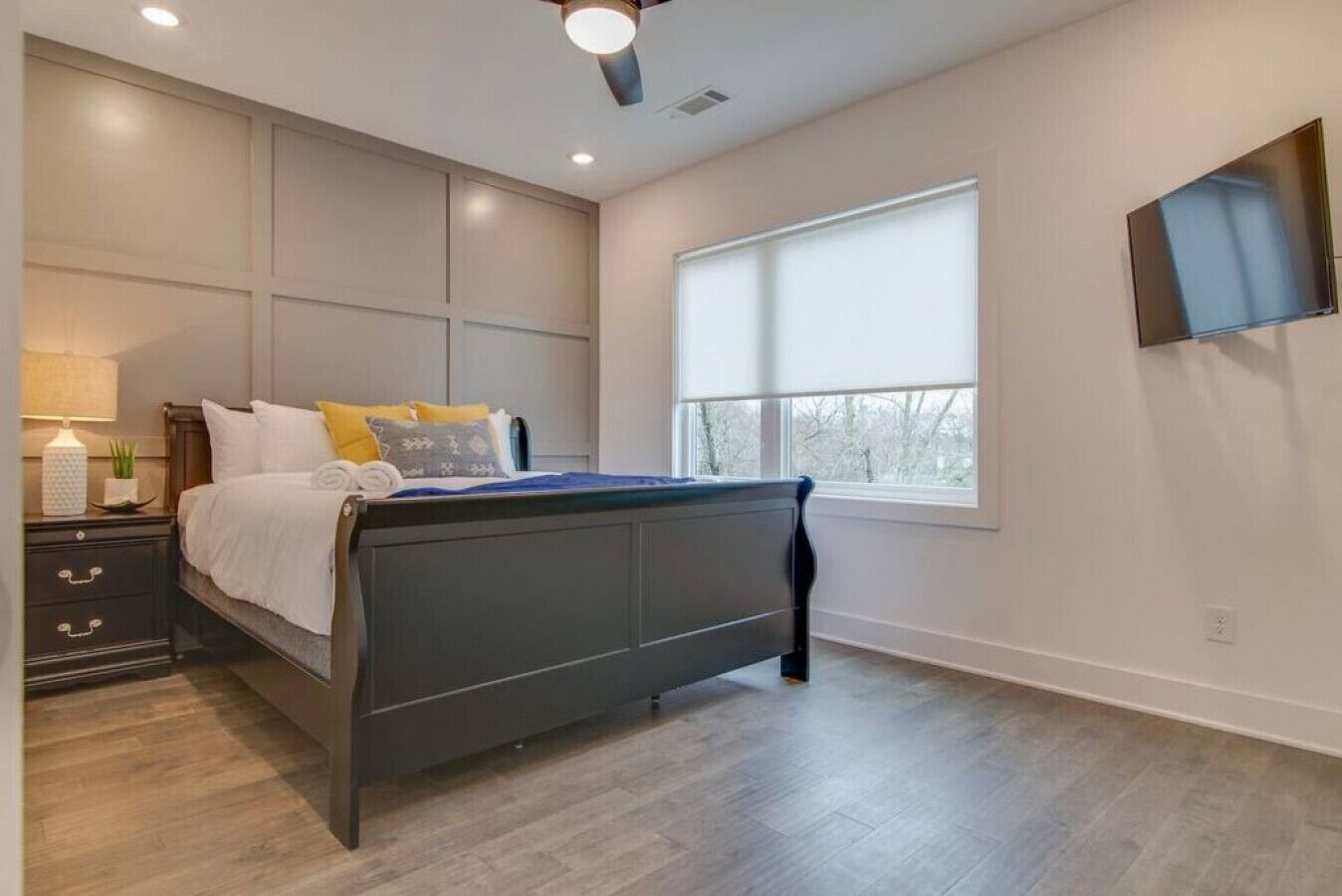 A bedroom with a bed, bedside table, lamp, and a window with blinds.