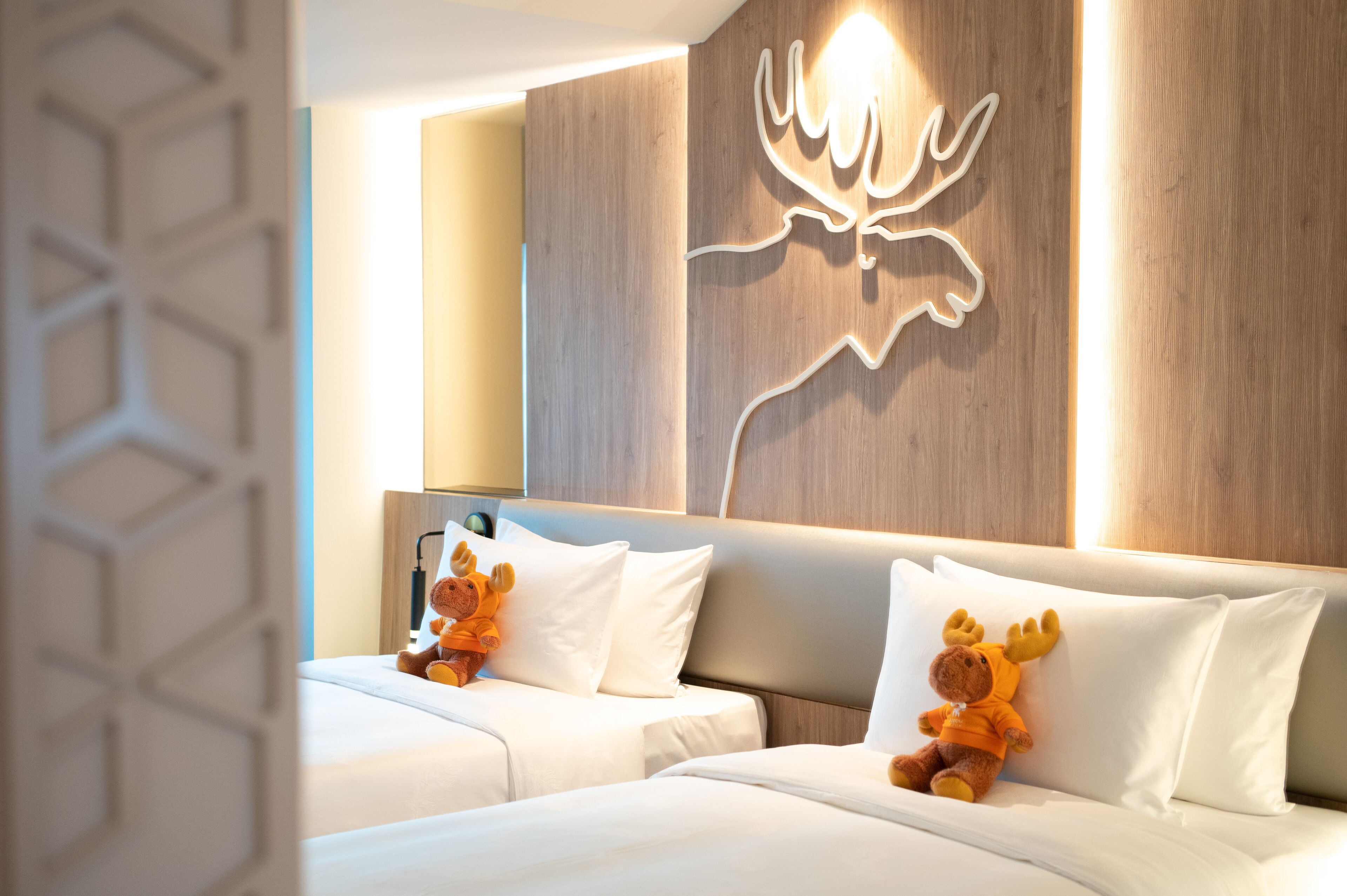 A hotel room with a modern design, featuring a large bed with white bedding and two plush toys on it.