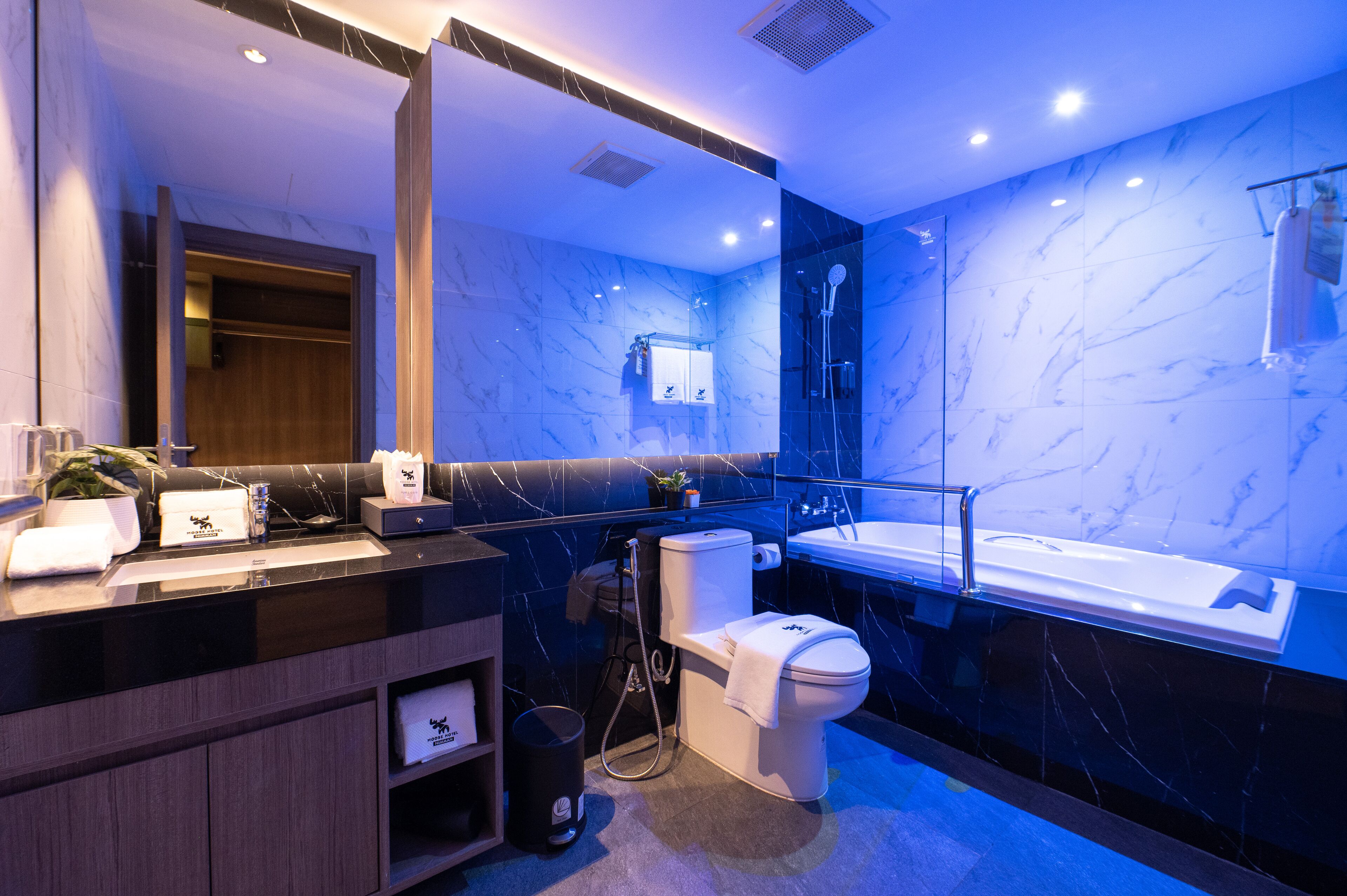 A modern bathroom with a black marble vanity, a toilet, a bathtub, and a large mirror.