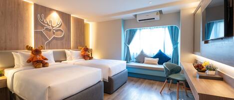 A modern hotel room with two beds, a seating area with a view, and a small desk with a plant and fruit bowl.
