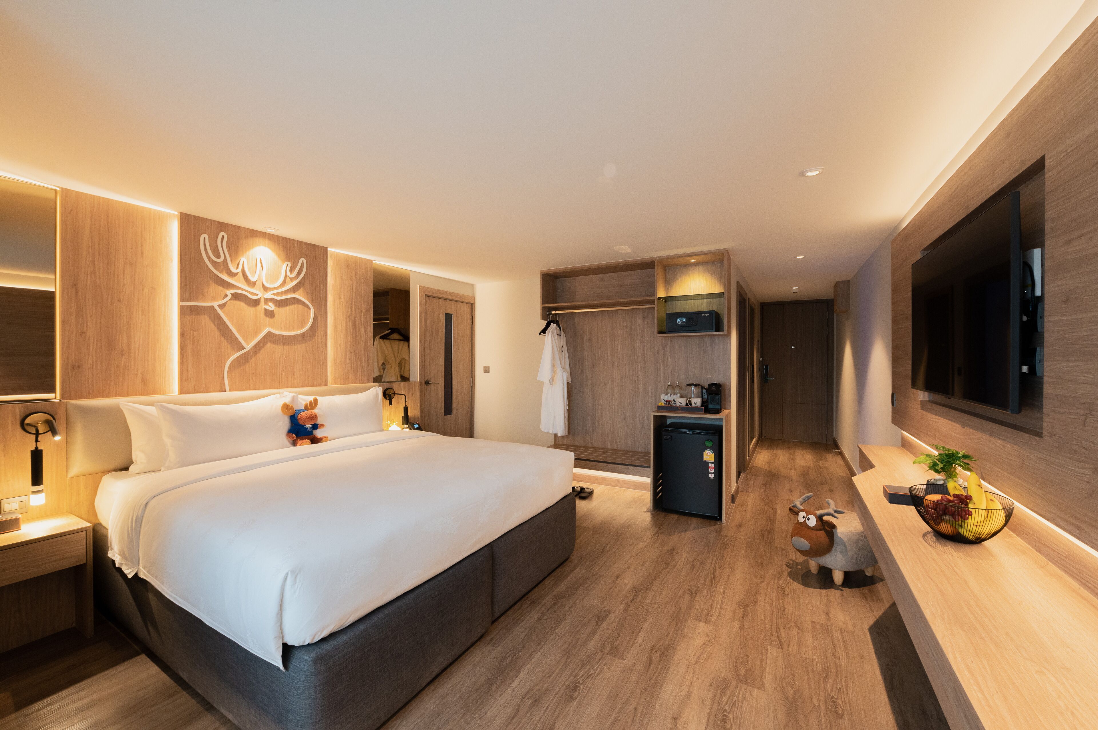 Een moderne hotelkamer met een groot bed, een kleine koelkast, een televisie en een houten wandpaneel.