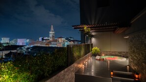 En tagterrasse med jacuzzi, pergola og byudsigt i baggrunden.