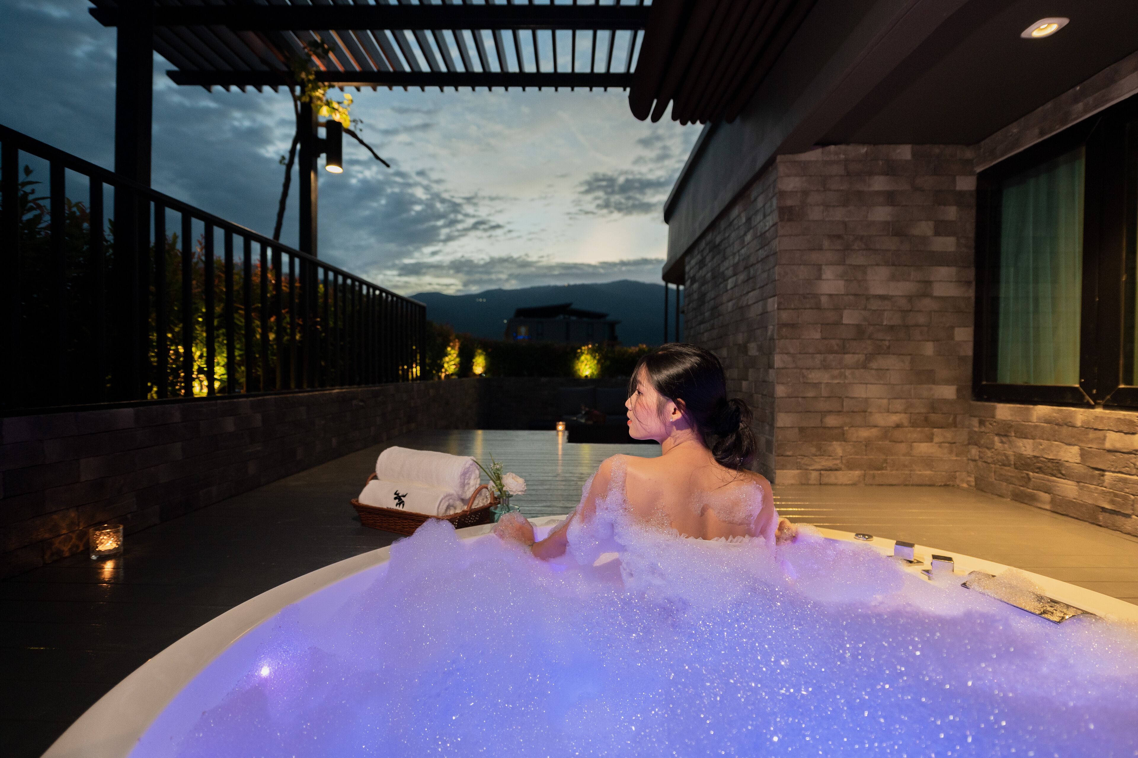 A person relaxing in a hot tub with a view of mountains and a building in the background.