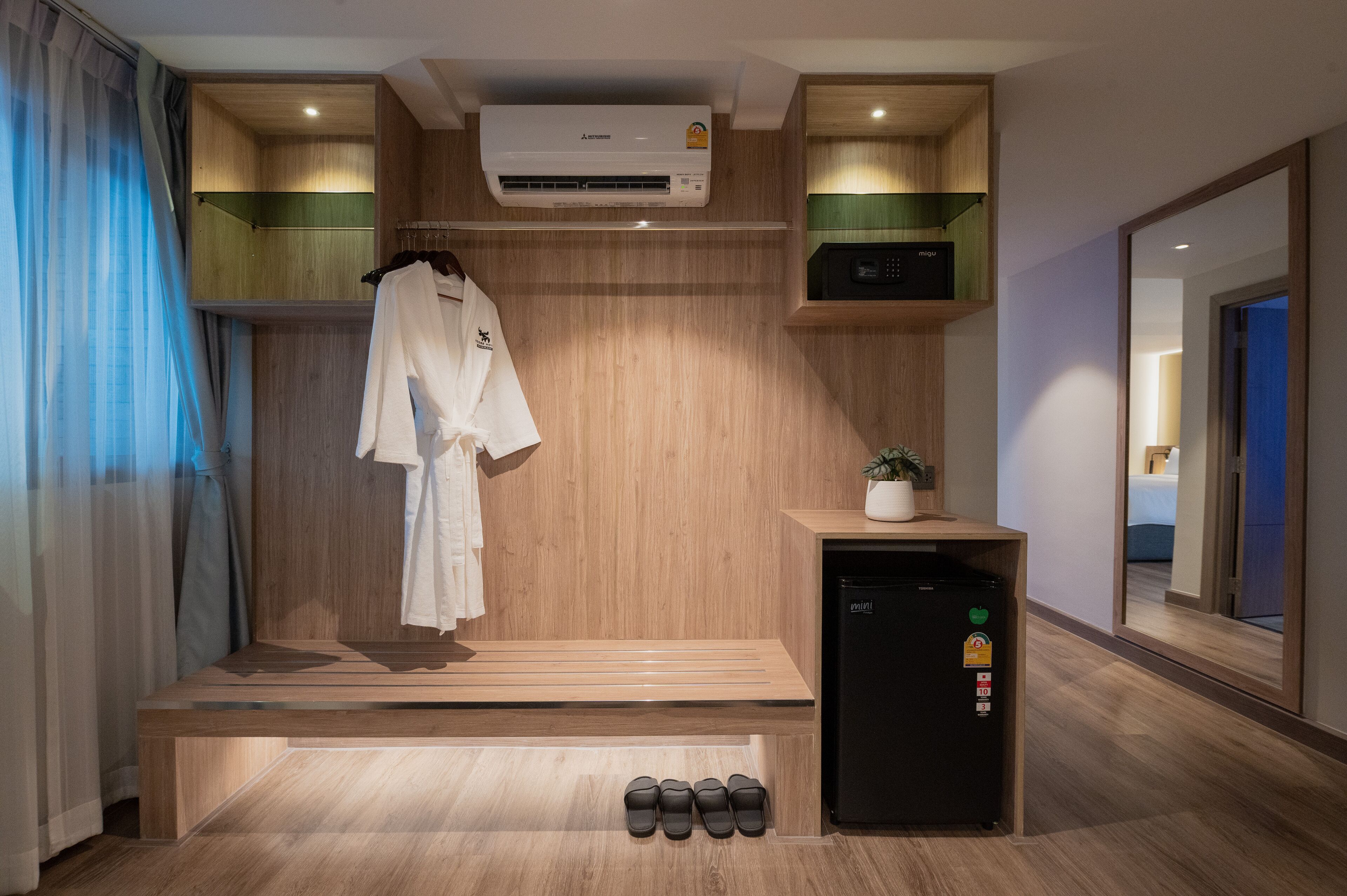 A modern bathroom with a wooden vanity, a towel rack, a small refrigerator, and a bench.