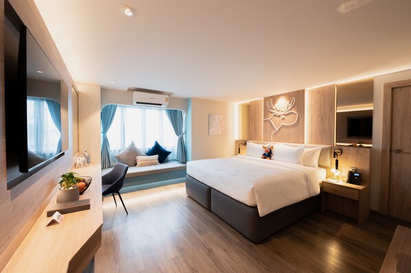 A modern hotel room with a large bed, a seating area with a view, a flat-screen TV, and a wooden desk with a plant. - Moose Hotel Nimman (Chiang Mai)