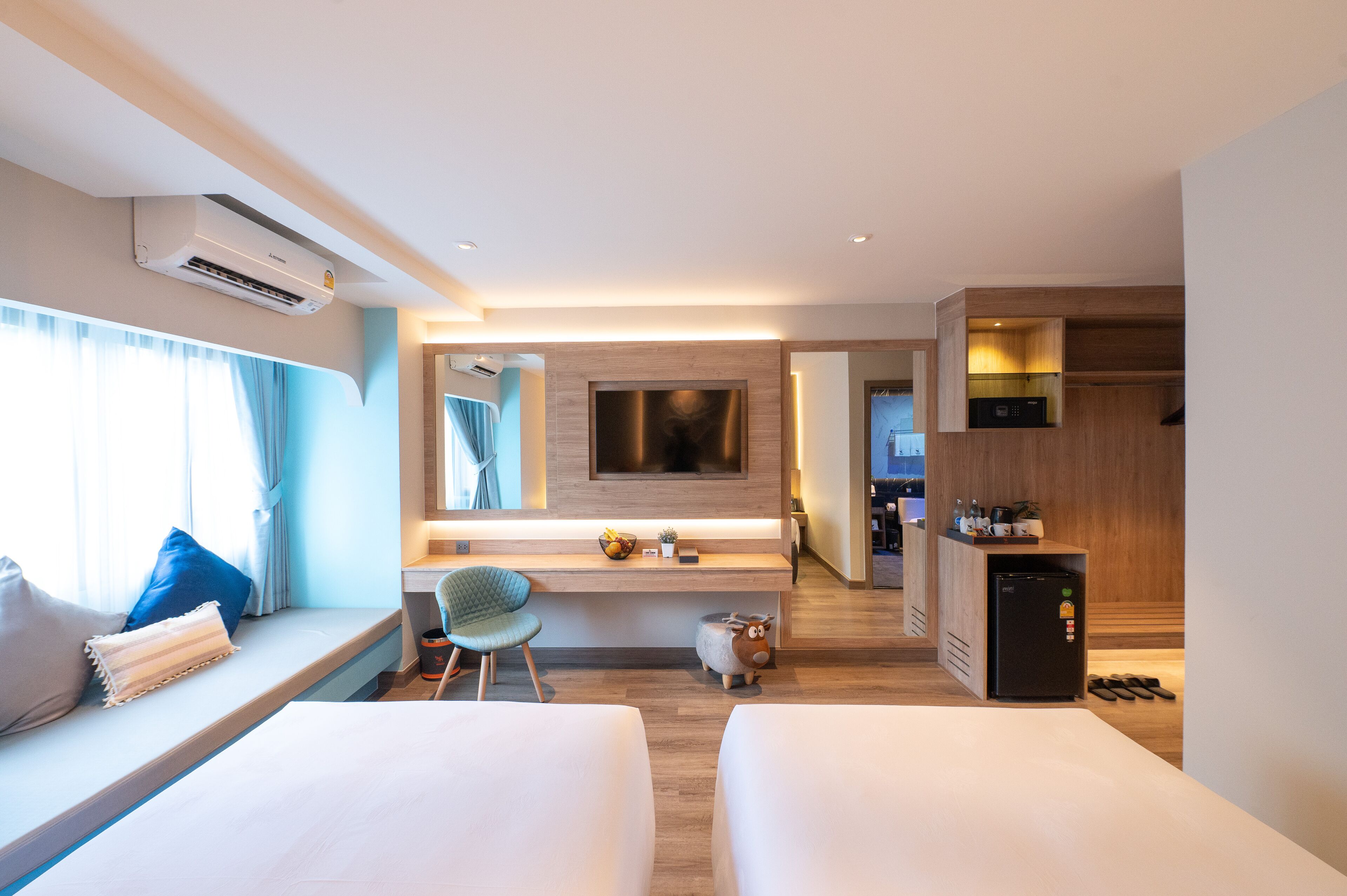 A modern hotel room with a sofa, a small table, a TV, a mini-fridge, and a kitchen area.