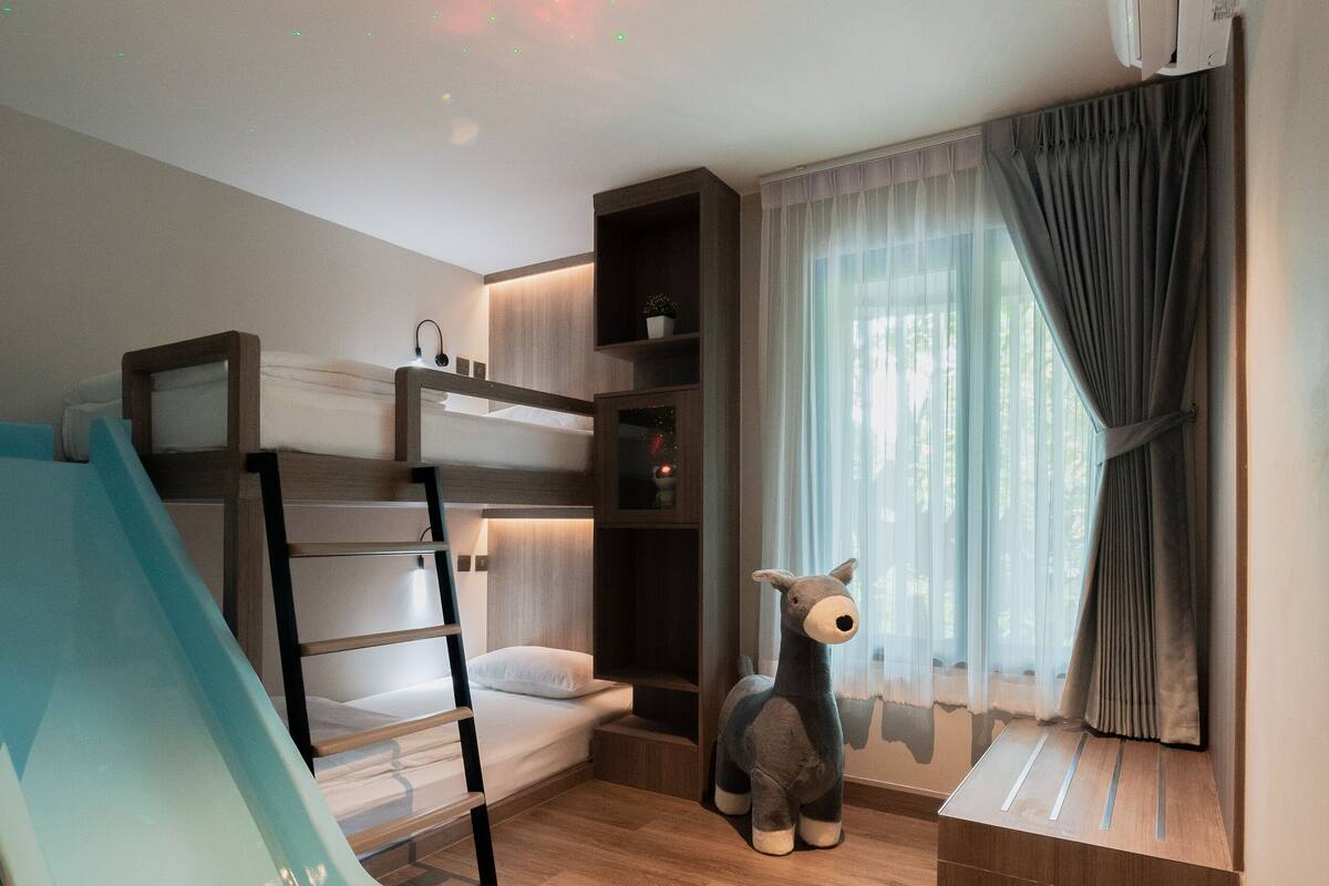A room with a bunk bed, a slide, a stuffed toy, and a window with curtains.