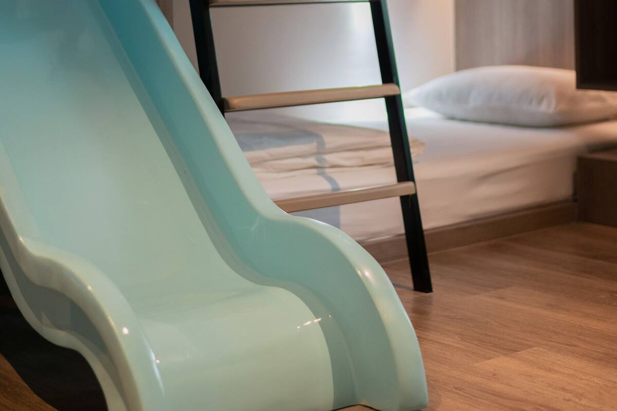 A bunk bed with a ladder, a light blue slide, and a bedside table.