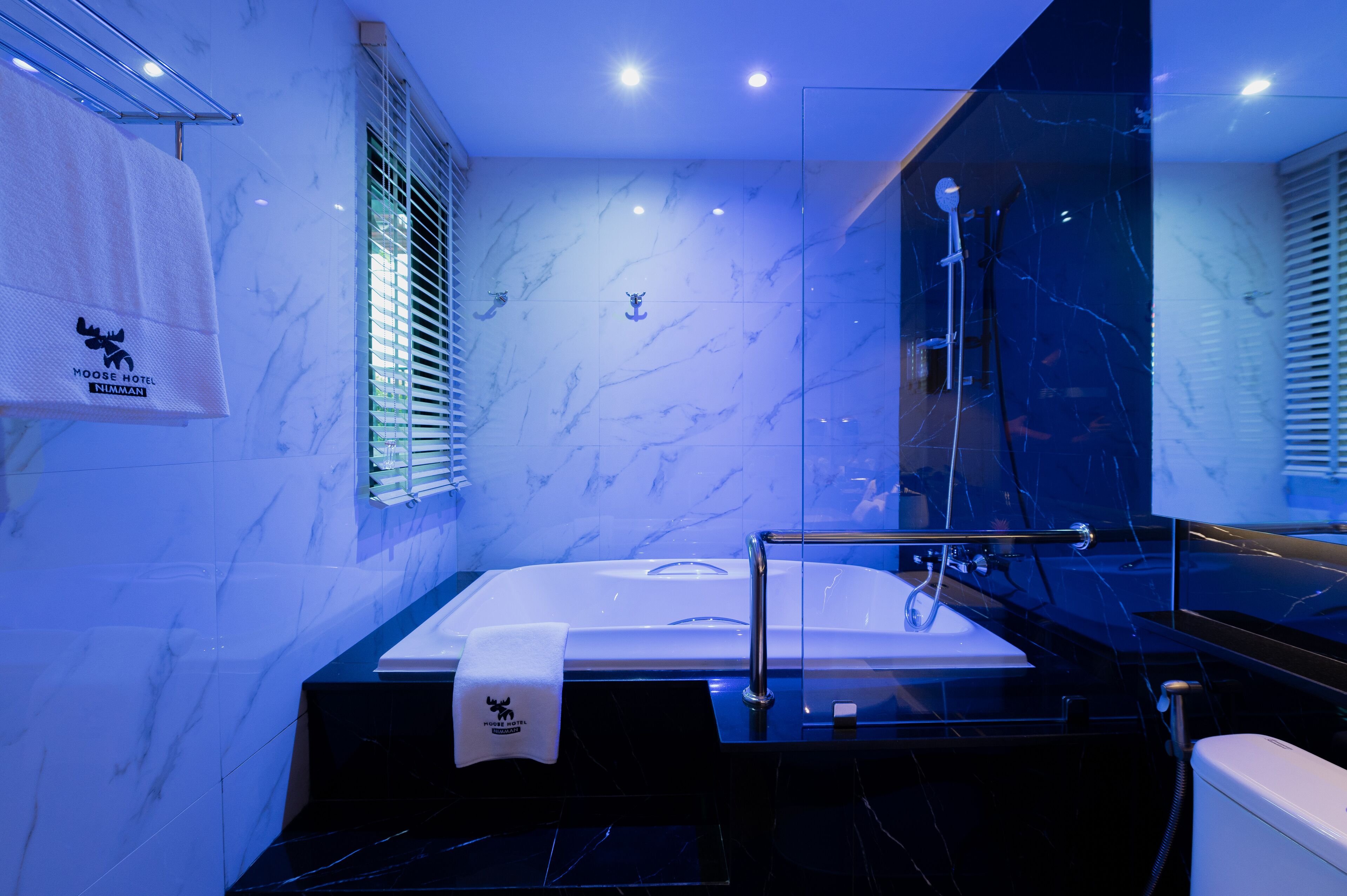A modern bathroom with a marble wall, a large bathtub, a glass shower enclosure, and a towel rack with a towel.