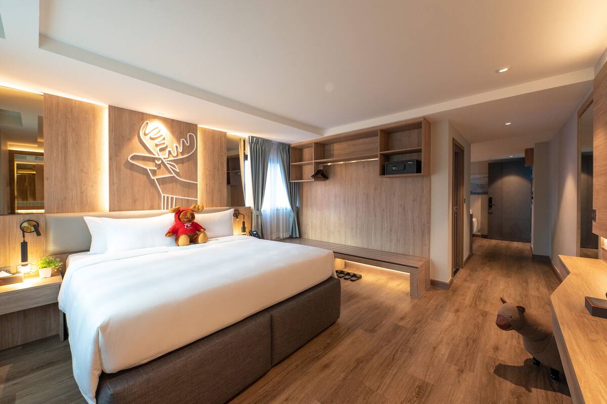 A modern hotel room with a large bed, bedside tables, a wardrobe, and a mirror.