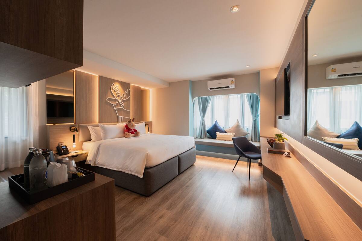 A modern hotel room with a large bed, bedside tables, a desk, and a window with curtains.