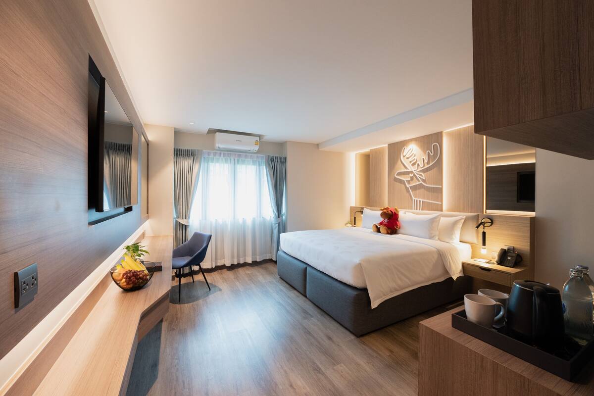A modern hotel room with a large bed, bedside table, and a desk with a chair.
