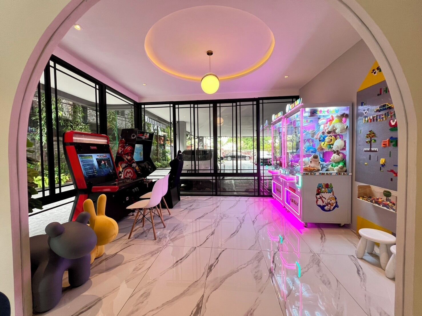 A modern gaming room with arcade machines, plush toys, and a neon-lit claw machine.