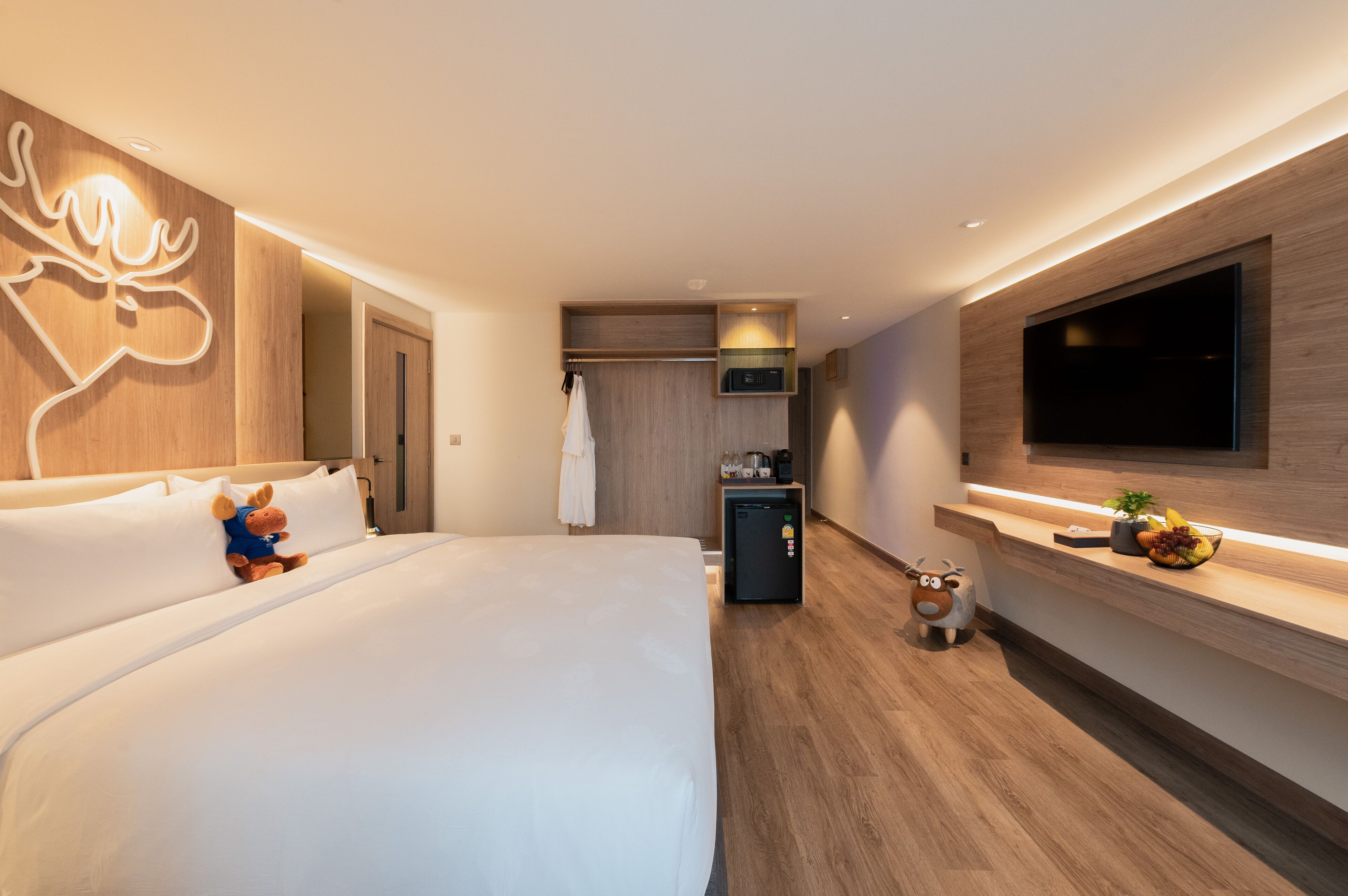 Une chambre d’hôtel moderne dotée d’un grand lit, d’un téléviseur à écran plat fixé au mur, d’un petit réfrigérateur et d’un mur décoratif en bois agrémenté d’un luminaire.