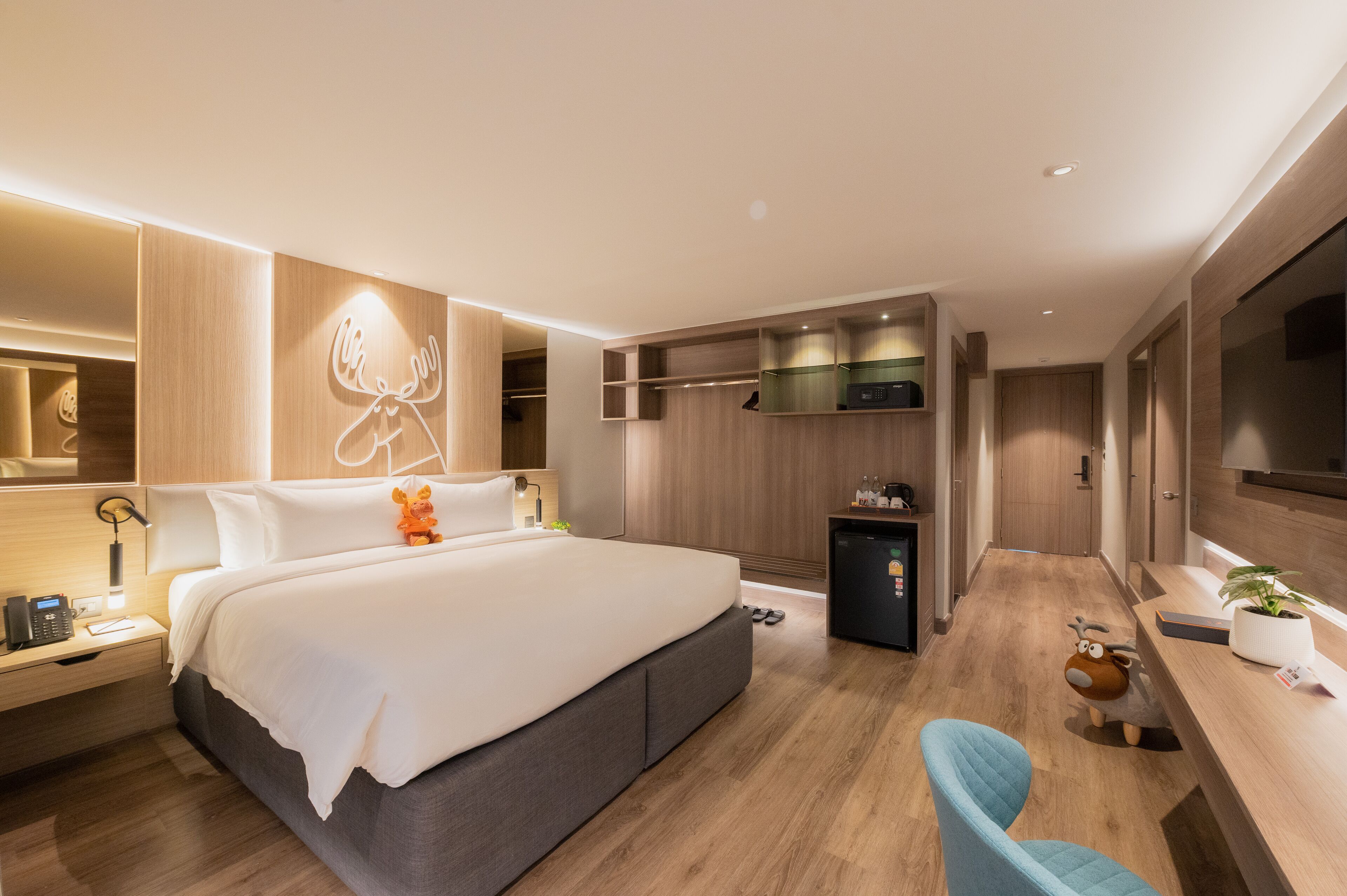 Una habitación de hotel moderna con una cama grande, mesita de noche, lámpara y un refrigerador pequeño.