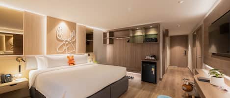 Una habitación de hotel moderna con una cama grande, mesita de noche, lámpara y un refrigerador pequeño.