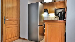 Una cocina con armarios de madera, un refrigerador de acero inoxidable, un microondas y una tetera.