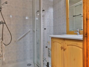 Eine Dusche mit Glastür, ein weißes Waschbecken und Holzschränke.