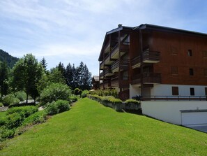Un immeuble à plusieurs étages doté de balcons, entouré d’une pelouse bien entretenue et d’arbres.