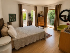 A bedroom with a bed, a dresser, a chair, a mirror, and a window with curtains.
