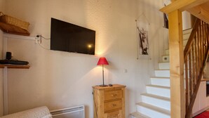 Ett sovrum med en säng, en byrå i trä, en röd lampa, en tv som är monterad på väggen och en trappa.