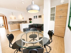 A modern kitchen with a round glass table and chairs, a wooden cabinet, and a dining area with a sofa.