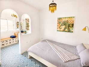 A bedroom with a bed, a chandelier, a window, and a wall with a painting.