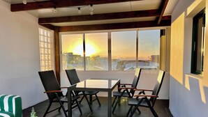Una habitación con una mesa, sillas, un farol verde y ventanas amplias que dan a una vista de la ciudad.