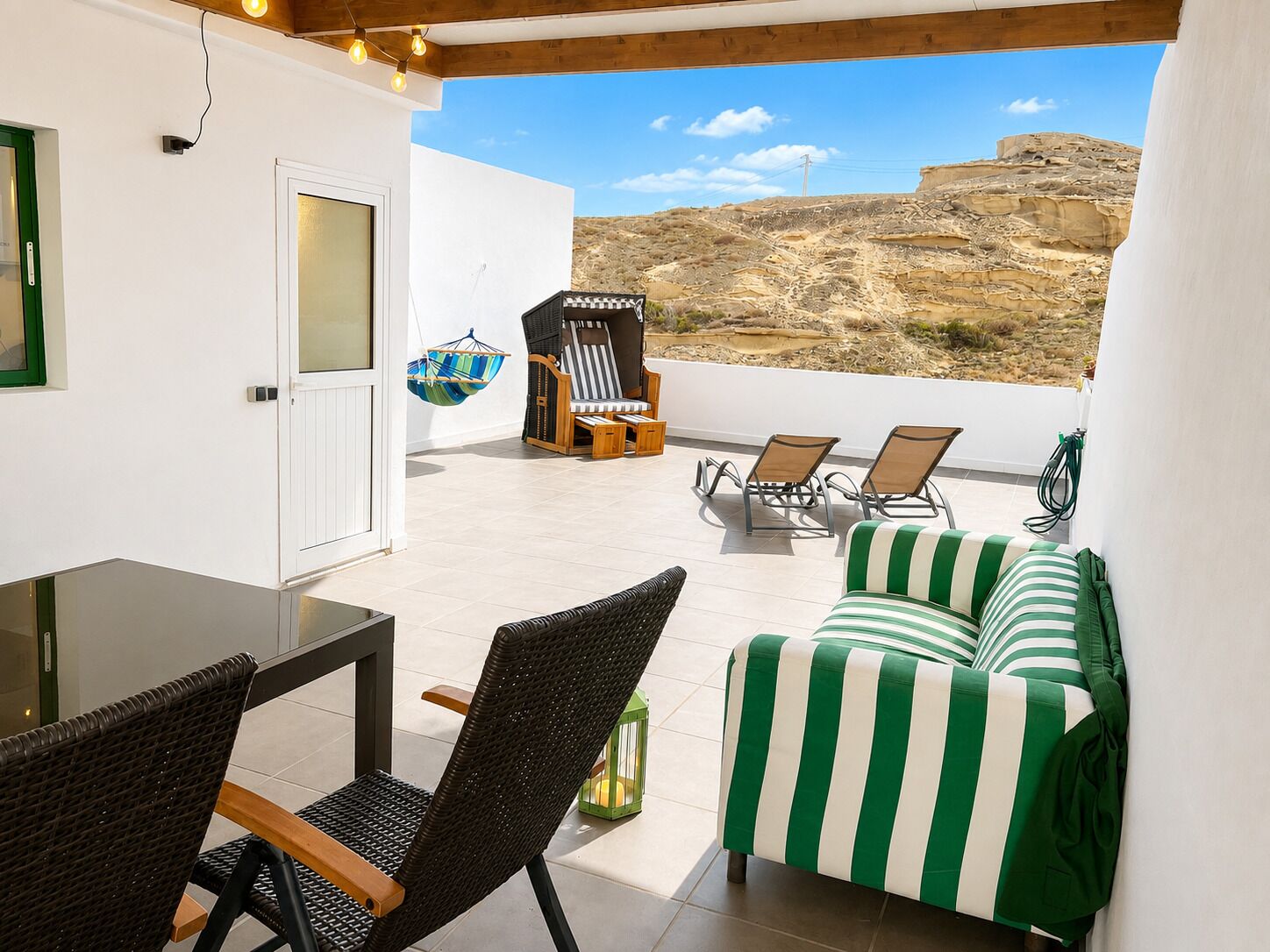 A balcony with wicker furniture, a striped sofa, and a hanging chair.