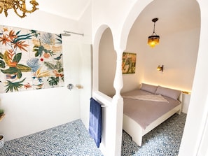 A room with a bed, a shower, a wall with a tropical mural, and an arched doorway. - Large quiet terrace. Only 150 m to the sea. (La Caleta)