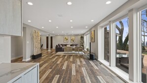 Un salon spacieux avec un grand canapé, une table basse et une cheminée. De grandes fenêtres offrent une vue sur l’extérieur.