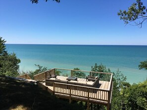 A wooden deck with outdoor seating overlooking a clear blue sea.