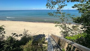 Une terrasse en bois qui mène à une plage bordée d’une eau d’un bleu limpide et où l’on aperçoit la terre ferme au loin.