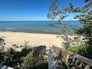 Une terrasse en bois qui mène à une plage bordée d’une eau d’un bleu limpide et où l’on aperçoit la terre ferme au loin.