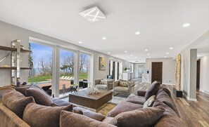 Amplia sala de estar con un sofá modular grande, una mesa de centro y vistas al exterior a través de amplios ventanales.