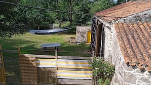 Un edificio de piedra con techo de tejas, cerca de madera y un patio cubierto de césped con un trampolín y una mesa.