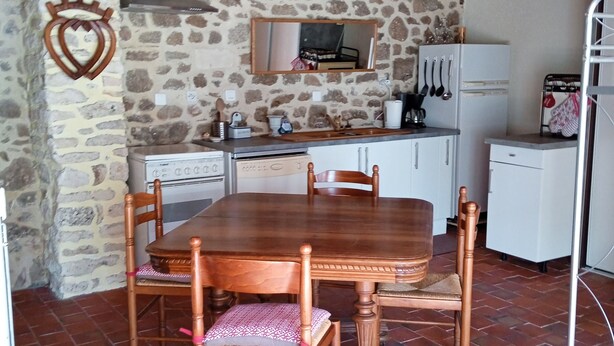 Una cocina rústica con pared de piedra, vigas de madera en el techo, suelo de baldosas y una mesa de comedor de madera con sillas.