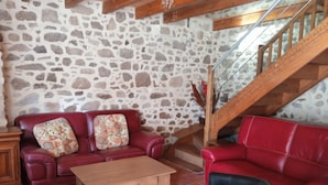 Un salón con pared de piedra, escaleras de madera y sofás de cuero rojo.