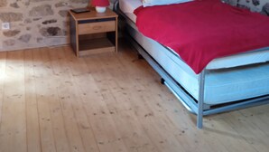 Un dormitorio con pared de piedra, techo de madera, estructura de cama de metal y mesita de noche de madera con una lámpara.