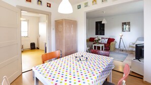 Un comedor con mantel a lunares, una lámpara colgante blanca y un sofá rojo al fondo.