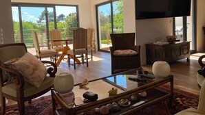 A spacious living room with a large glass table, comfortable seating, and a flat-screen TV.