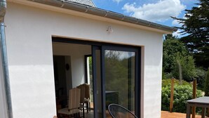A covered outdoor patio with a wicker chair and a small table, a sliding glass door leading to an interior space, and a wooden deck.