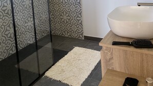 A modern bathroom with a glass shower enclosure, a large bathtub, and patterned tiles.