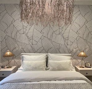 Modern bedroom with geometric patterned wallpaper, a bed, and two bedside tables with lamps and clocks.
